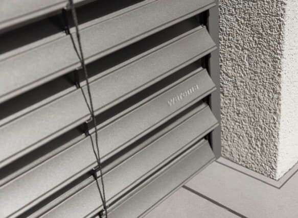 Graue Außenjalousien als Sonnenschutz am Wohnhausfenster